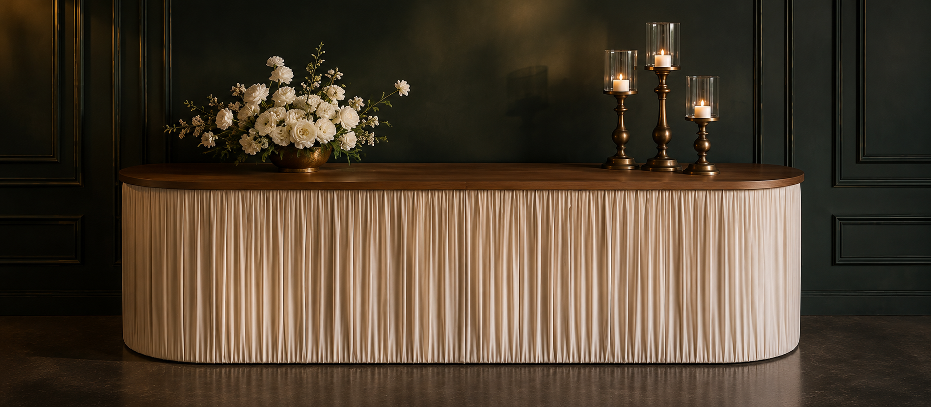 Oval entry table with pleated ivory fabric base styled with white florals and brass candlesticks against forest green wall