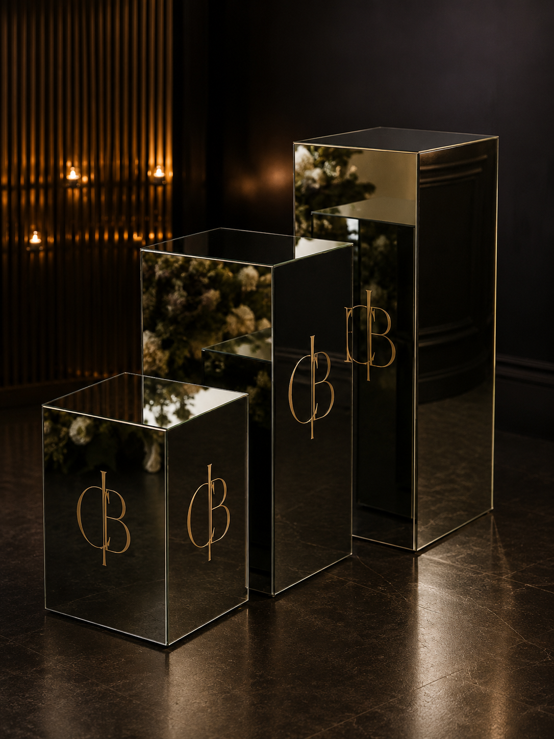 Three mirrored pedestal boxes with gold monogram lettering in heights 24, 36, and 48 inches